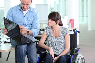 Pige i kørestol ser på computerskærm sammen med en ung mand